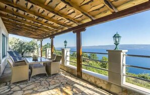 A covered outdoor seating area with stone flooring, a table, and chairs, overlooking a scenic view of the sea. - Lovely home in Jesenice with sauna (Jesenice)