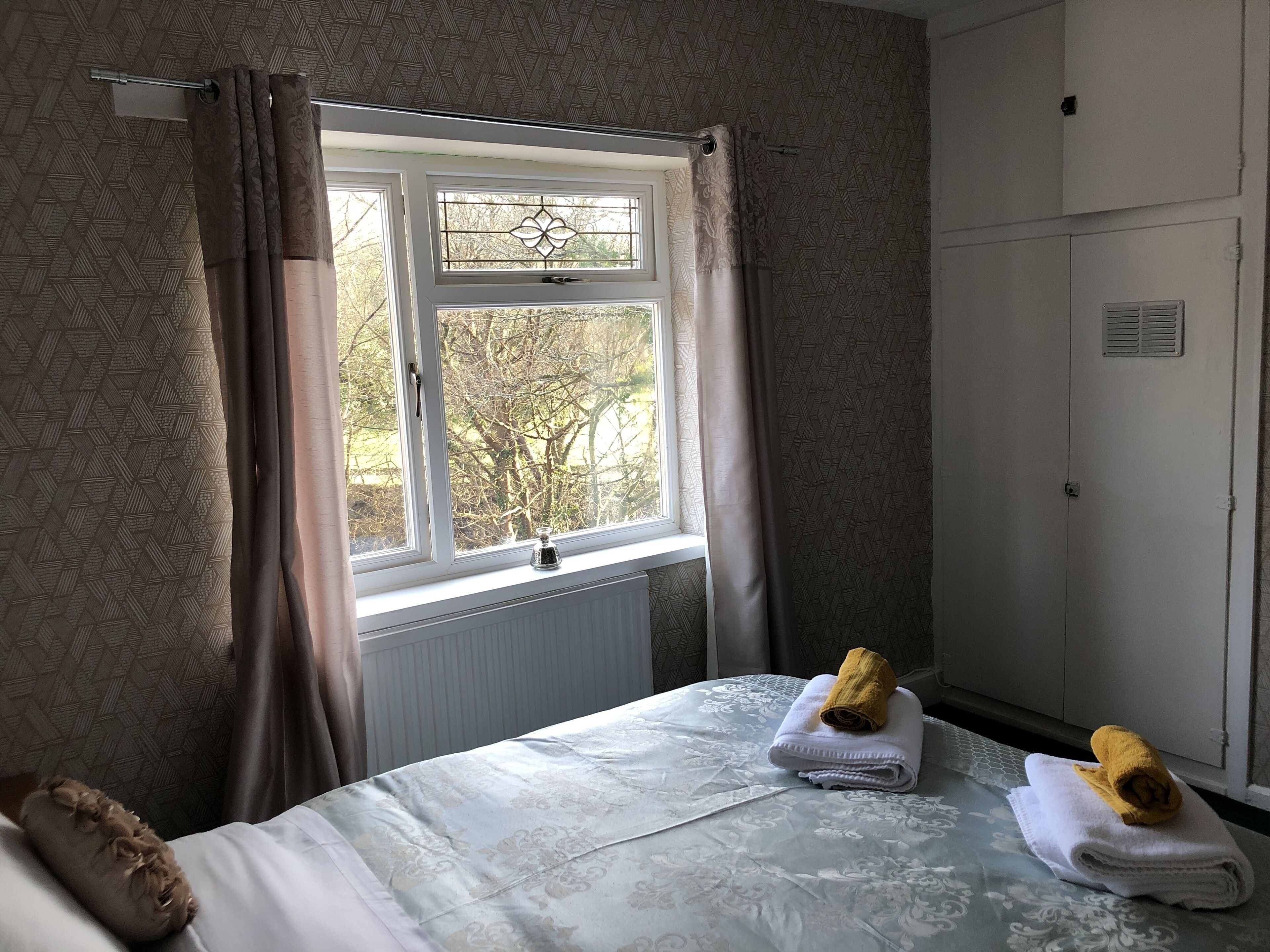 A hotel room with a bed, a window with curtains, a radiator, and a wardrobe.