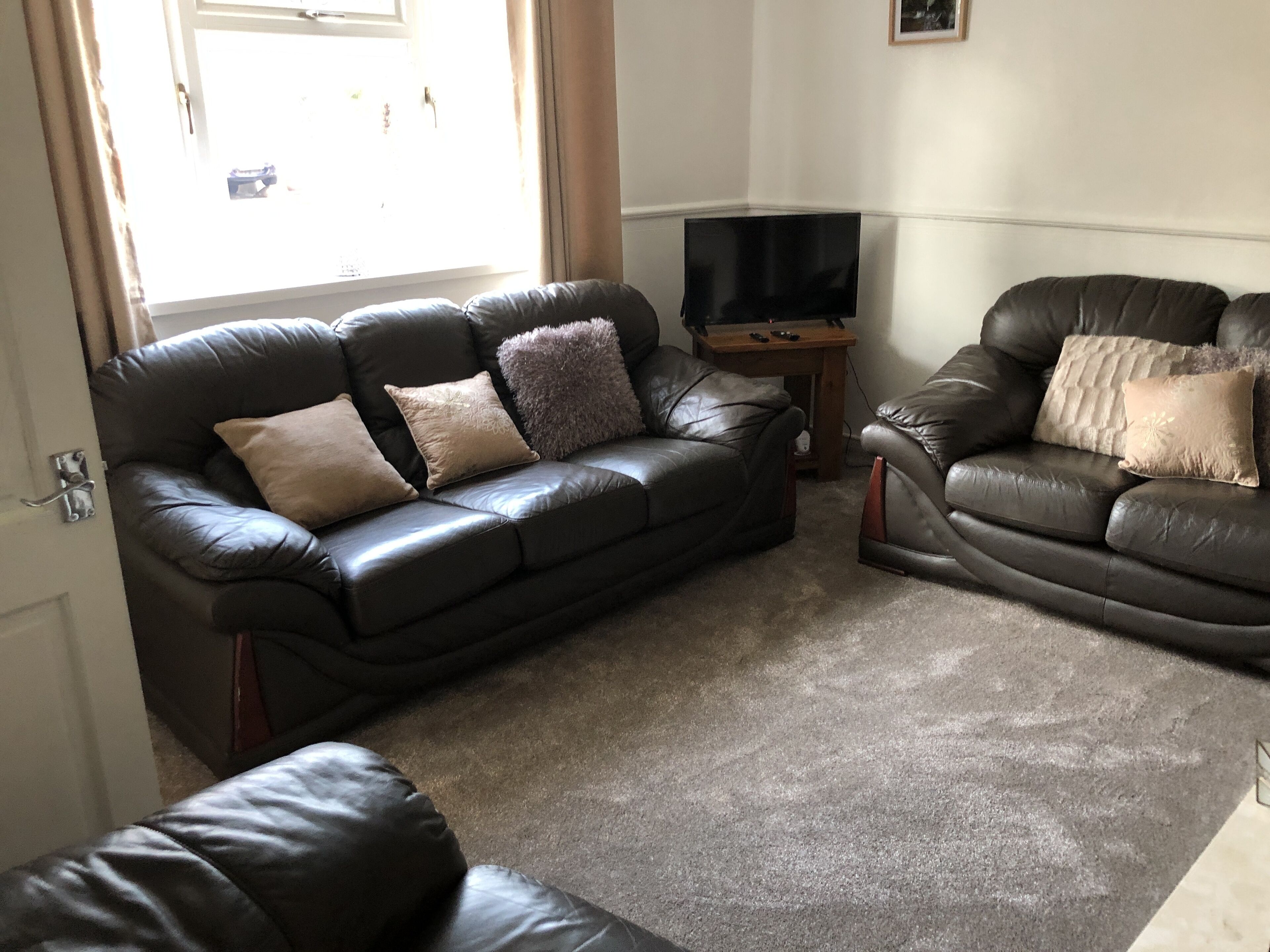 A living room with two leather sofas, a flat-screen TV, and a small wooden table.