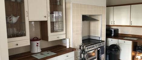 A kitchen with white cabinets, a stainless steel range hood, a microwave, and a trash bin.