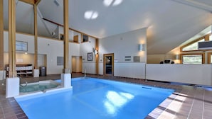 A large indoor swimming pool with a clear blue water surface, surrounded by a tiled floor and walls, and a wooden ceiling structure. - Trail Creek 12 on the ski back trail with an indoor pool Next to Golf course (Killington)