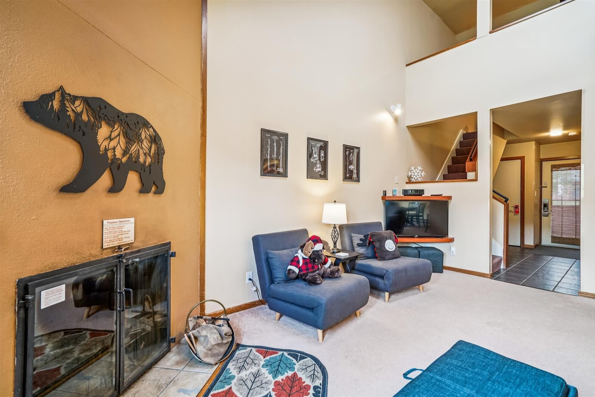 Uma sala de estar com lareira, dois sofás, uma televisão e uma decoração de urso na parede.