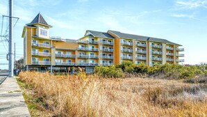 A multi-story hotel with balconies, a tower-like structure, and a grassy foreground. - Playa Flamingo 104-Bayside 83rd St, Free WiFi, Pool, Elev, W/D, AC (Ocean City)