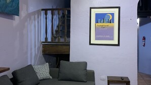 Een woonkamer met een grijze modulaire bank, een klein houten tafeltje, een ingelijst schilderij aan de muur en een trap naar een hoger niveau.