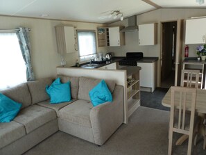Un espacio habitable compacto con kitchenette, un sofá con cojines azules y una zona de comedor.