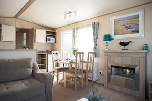 A compact living space with a sofa, dining table, chairs, a fireplace, and a kitchen area with a microwave.