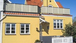Een geel gebouw met een rode pannendak, witte ramen en een witte hekwerk.
