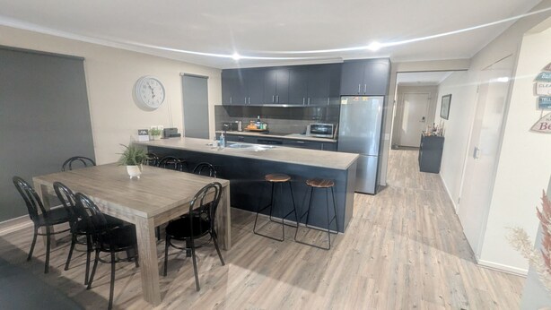 Une cuisine moderne avec des meubles de couleur sombre, un îlot central et un coin repas comprenant une table et des chaises en bois.