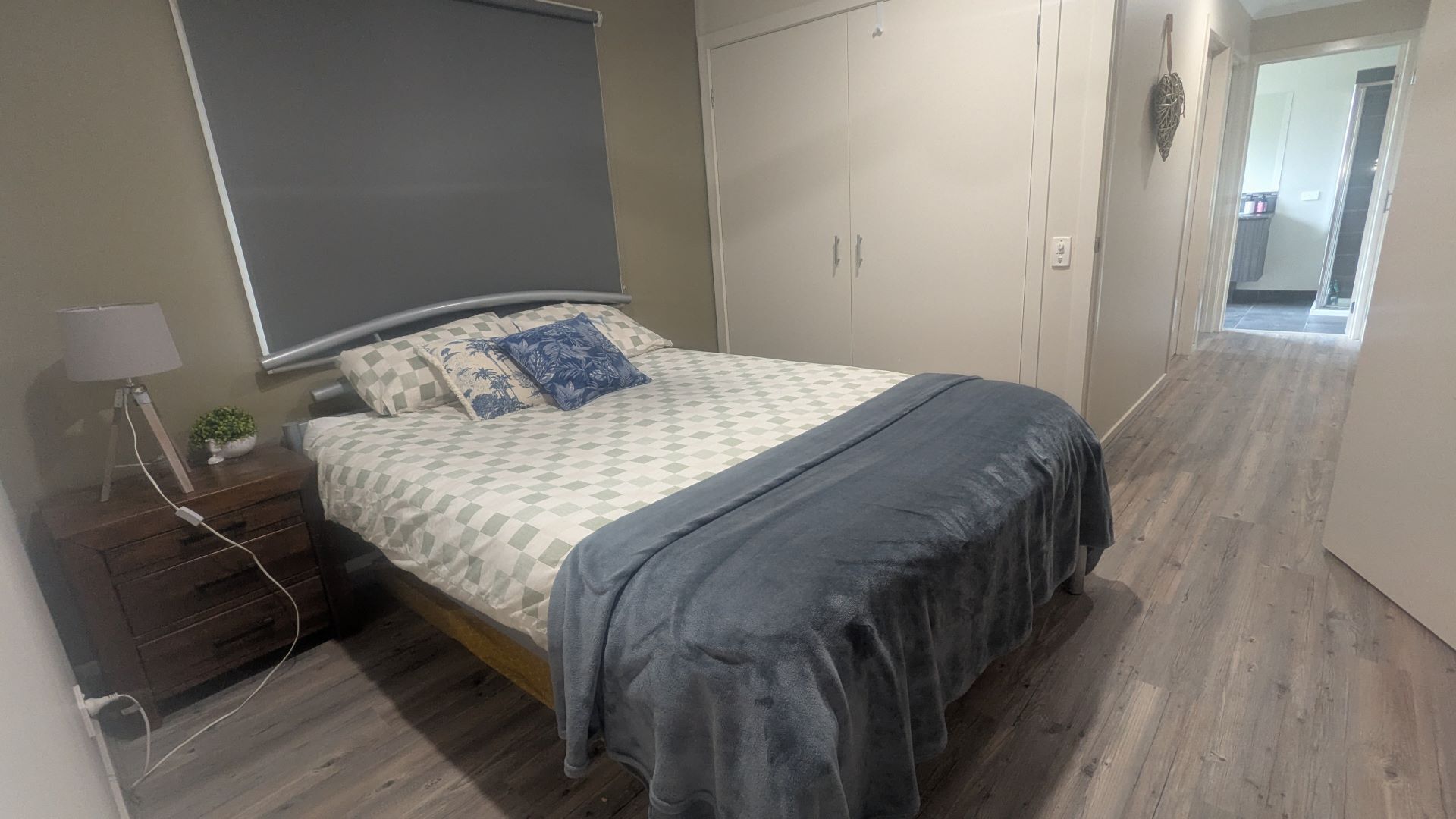 Ein Schlafzimmer mit Bett, Nachttisch mit Lampe, einer kleinen Pflanze und einem Kleiderschrank.