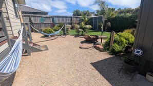 Un jardin avec un hamac, un foyer et une clôture en bois.