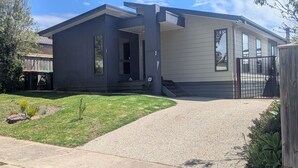 Une maison moderne à deux étages, dotée d’un porche couvert, d’un numéro « 2 » bien visible sur le côté et d’une allée d’accès fermée par un portail.