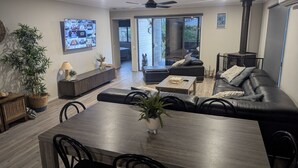 Un salon moderne avec un canapé en cuir foncé, une table à manger en bois et un téléviseur fixé au mur.
