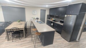 Une cuisine moderne dotée d’un îlot central, de meubles de rangement aux couleurs sombres et d’un coin repas avec une table et des chaises en bois.