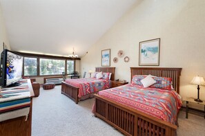 A bedroom with two beds, a TV, a desk, and a window with a view of trees and mountains.