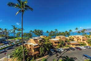 A coastal hotel with multiple-story buildings, a parking lot, and palm trees.