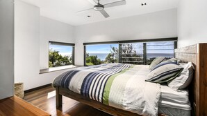 A bedroom with a bed, a ceiling fan, and large windows with a view of the sea. - Banyandah - Luxury Architect Designed Straddie Beachhouse (Point Lookout)