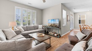 A living room with a sofa set, a coffee table, a TV on a stand, and a ceiling fan. - 6-Bedroom Surfside House with Private Pool and Beach Access (Surfside Beach)