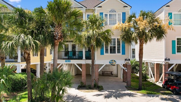 A beachfront property with a covered porch, palm trees, and a clear blue sky. - 6-Bedroom Surfside House with Private Pool and Beach Access (Surfside Beach)