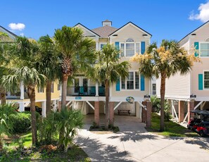 A beachfront property with a covered porch, palm trees, and a clear blue sky. - 6-Bedroom Surfside House with Private Pool and Beach Access (Surfside Beach)