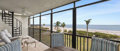 A balcony with a view of the beach, a spiral staircase, and a round table with a globe.