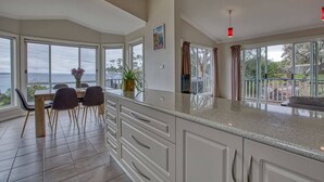 A spacious kitchen with large windows, a dining area with chairs, and a view of the sea. - Front Row Beachfront (Binalong Bay)
