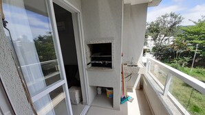 Un balcon avec une porte-fenêtre coulissante, un petit coin cuisine équipé d’un four à micro-ondes et d’un évier, et une vue sur la verdure et les bâtiments au loin.