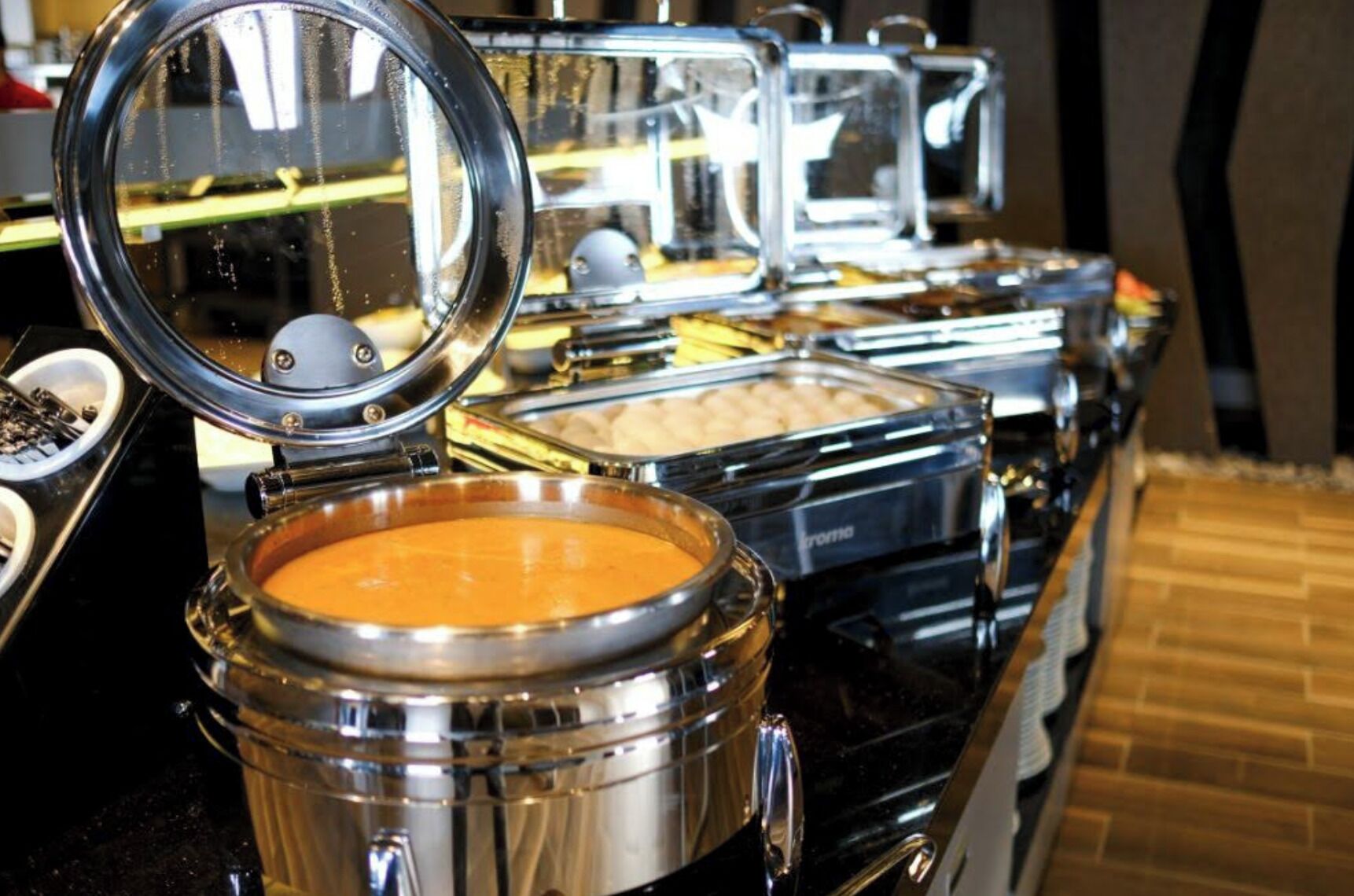 Un bufé con varios recipientes de comida, incluyendo un bol de sopa y un recipiente con la etiqueta 'TORTA'.