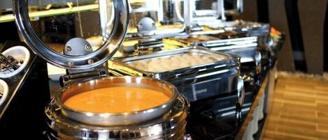 Un bufé con varios recipientes de comida, incluyendo un bol de sopa y un recipiente con la etiqueta 'TORTA'.