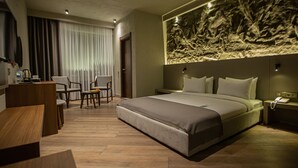 A modern hotel room with a large bed, a desk, two chairs, and a large abstract wall art piece. - The Erzurum Hotel (Erzurum)
