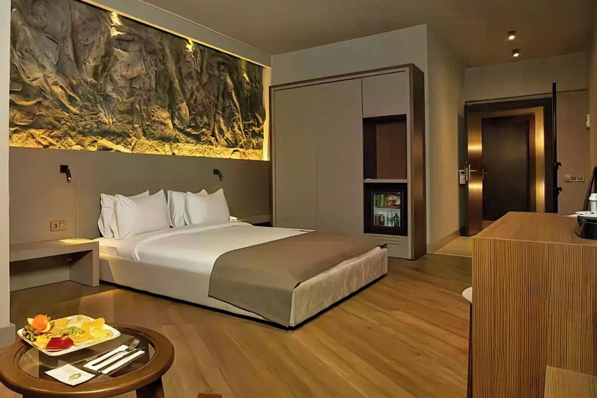 Une chambre d’hôtel moderne dotée d’un grand lit, d’une table à manger où le petit-déjeuner est servi, d’un minibar et d’une armoire.