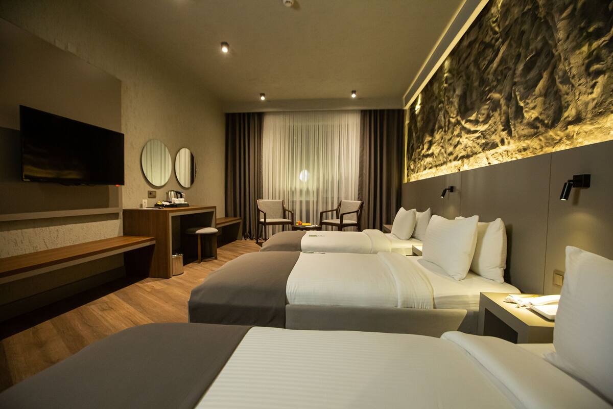Een hotelkamer met twee bedden, een bureau, stoelen, een televisie en een groot muurschilderij.