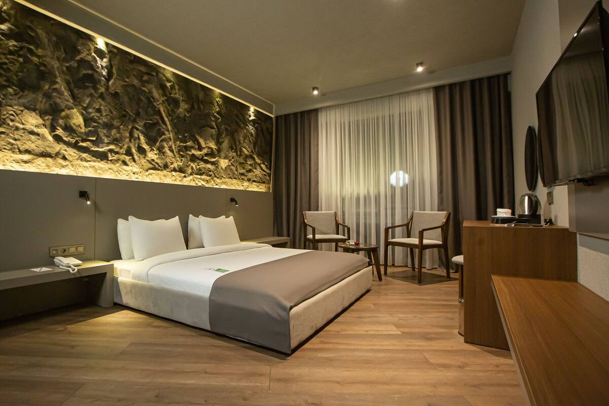 Een moderne hotelkamer met een groot bed, een bureau, een stoel, een televisie en een wand met een structuur.