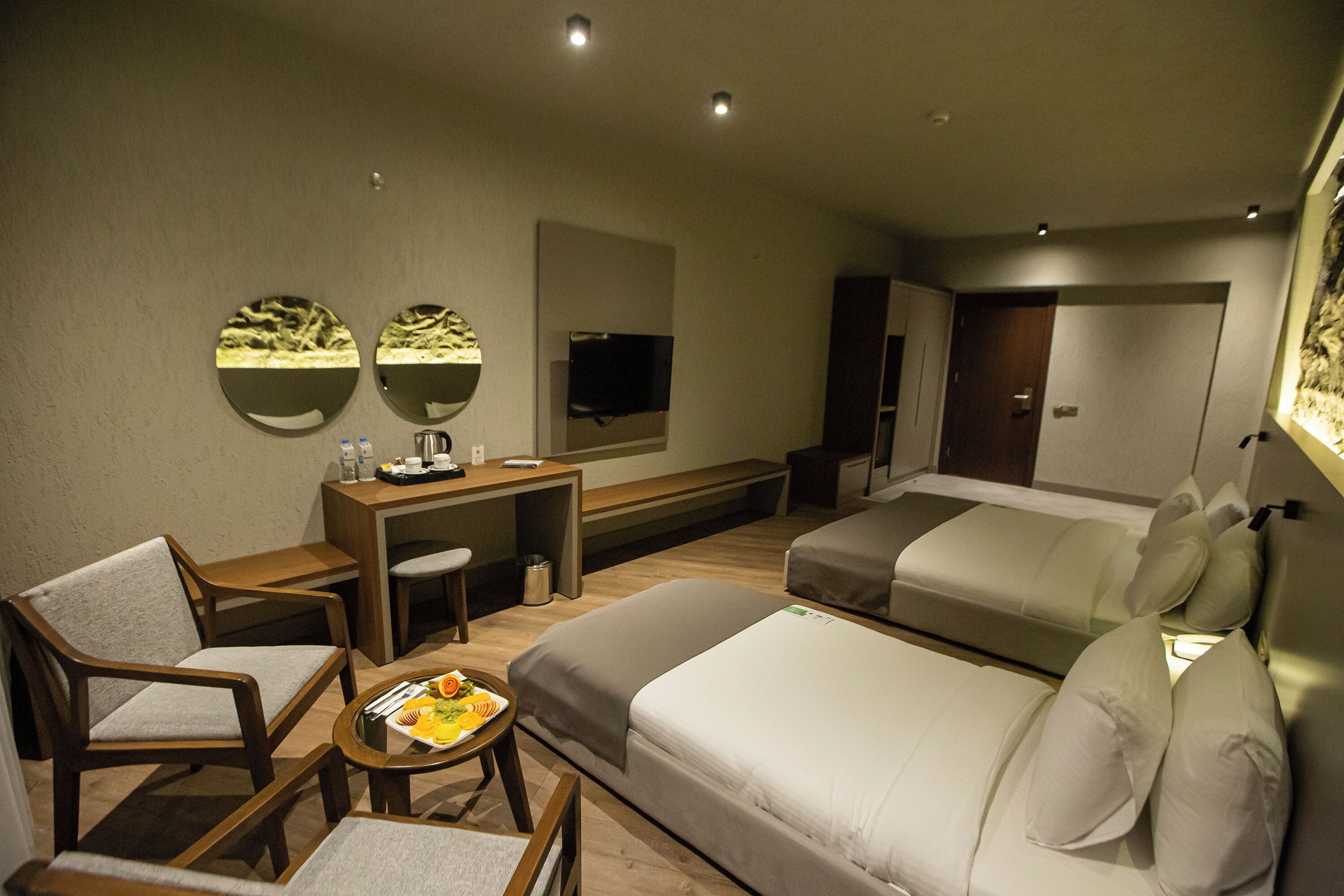 Hotelkamer met een bed, een bank, een bureau, een stoel, een televisie en een klein tafeltje met een schaal fruit.