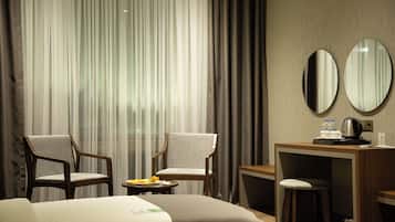 A hotel room with two chairs, a bed, a desk with a coffee maker, and a mirror.