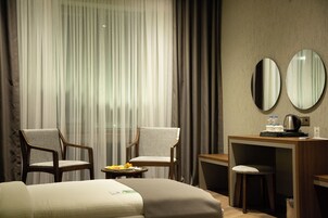 A hotel room with two chairs, a bed, a desk with a coffee maker, and a mirror.