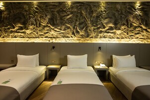 A hotel room with three beds, a textured wall, and a nightstand with a lamp.