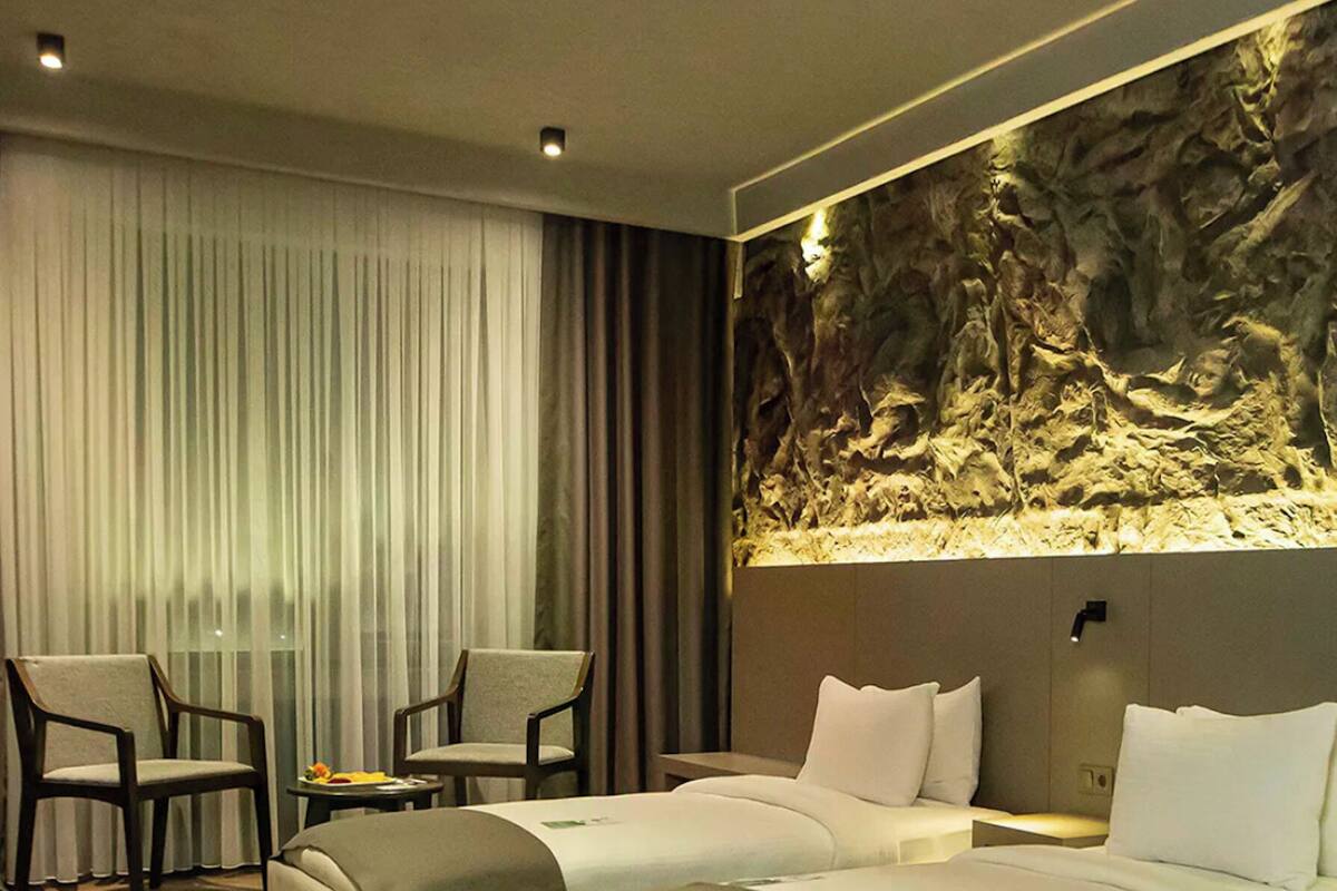Een hotelkamer met twee bedden, een zithoek met stoelen, een groot wandaquarium en een raam met gordijnen.