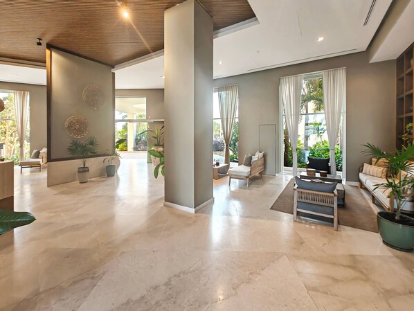 A spacious lobby with a high ceiling, marble flooring, and a seating area with a sofa and armchairs.
