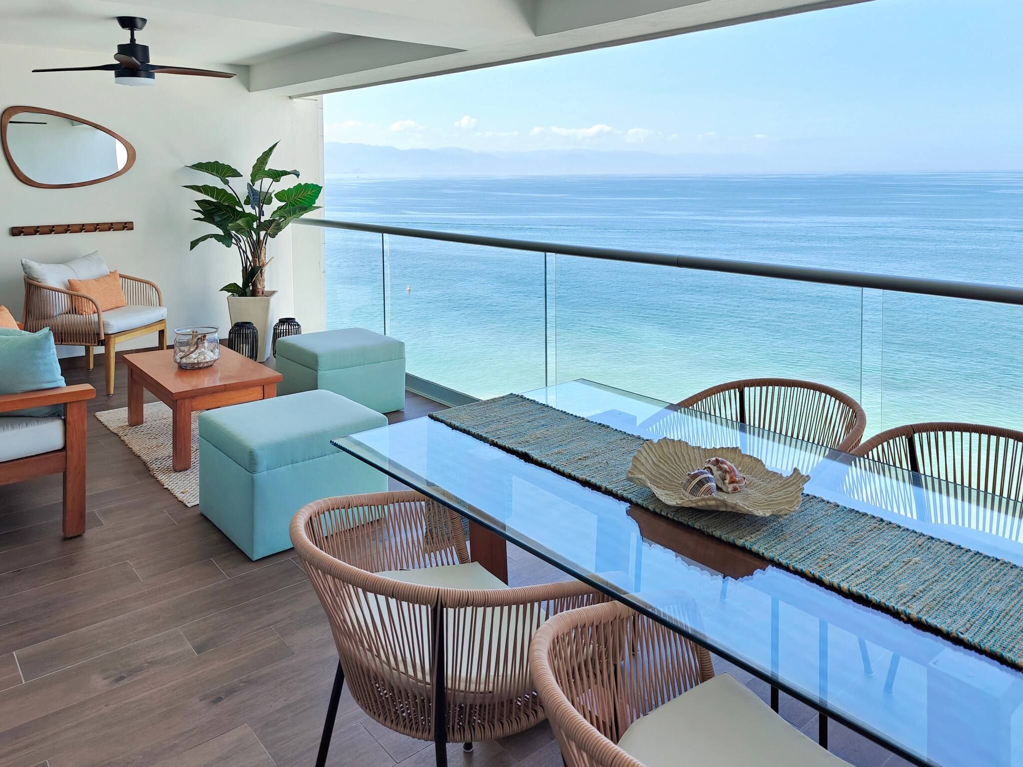 Een moderne woonkamer met een glazen tafel, rieten stoelen, een bank en uitzicht op de oceaan.