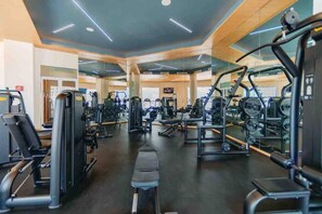 Et fitnesscenter med forskellige træningsmaskiner, spejle og en bænk i midten.