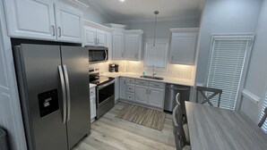 Una cucina moderna con mobili bianchi, elettrodomestici in acciaio inossidabile e un tavolo da pranzo in legno.