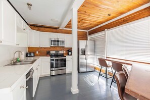 A modern kitchen with white cabinets, stainless steel appliances, and a wooden ceiling. - Commodore's Compound - One block from Duval St (Key West)