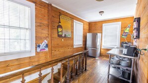 A kitchen with wooden walls, a stainless steel refrigerator, a wooden staircase, and a metal cart with dishes. - Commodore's Compound - One block from Duval St (Key West)