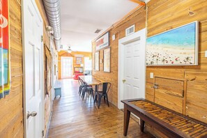 A hallway with wooden walls, a painting of a beach, and a table with chairs. - Commodore's Compound - One block from Duval St (Key West)