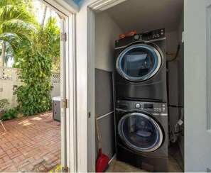A laundry room with two stacked washing machines, a mop, and a door leading to a garden.