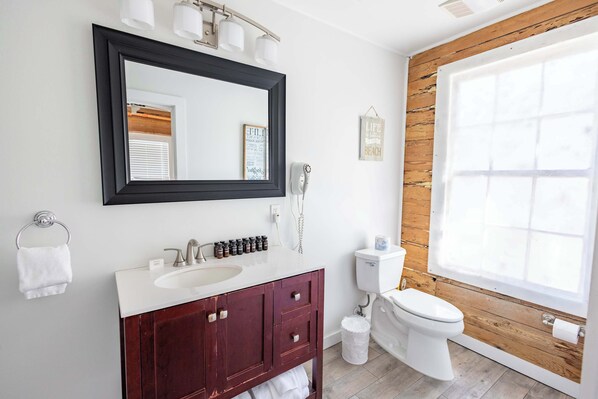 A bathroom with a wooden wall, a white sink, a mirror, a toilet, and a window.