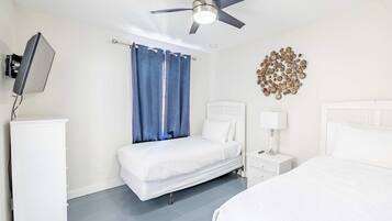 A hotel room with a bed, a bedside table with a lamp, a ceiling fan, a TV mounted on the wall, and a decorative wall piece.