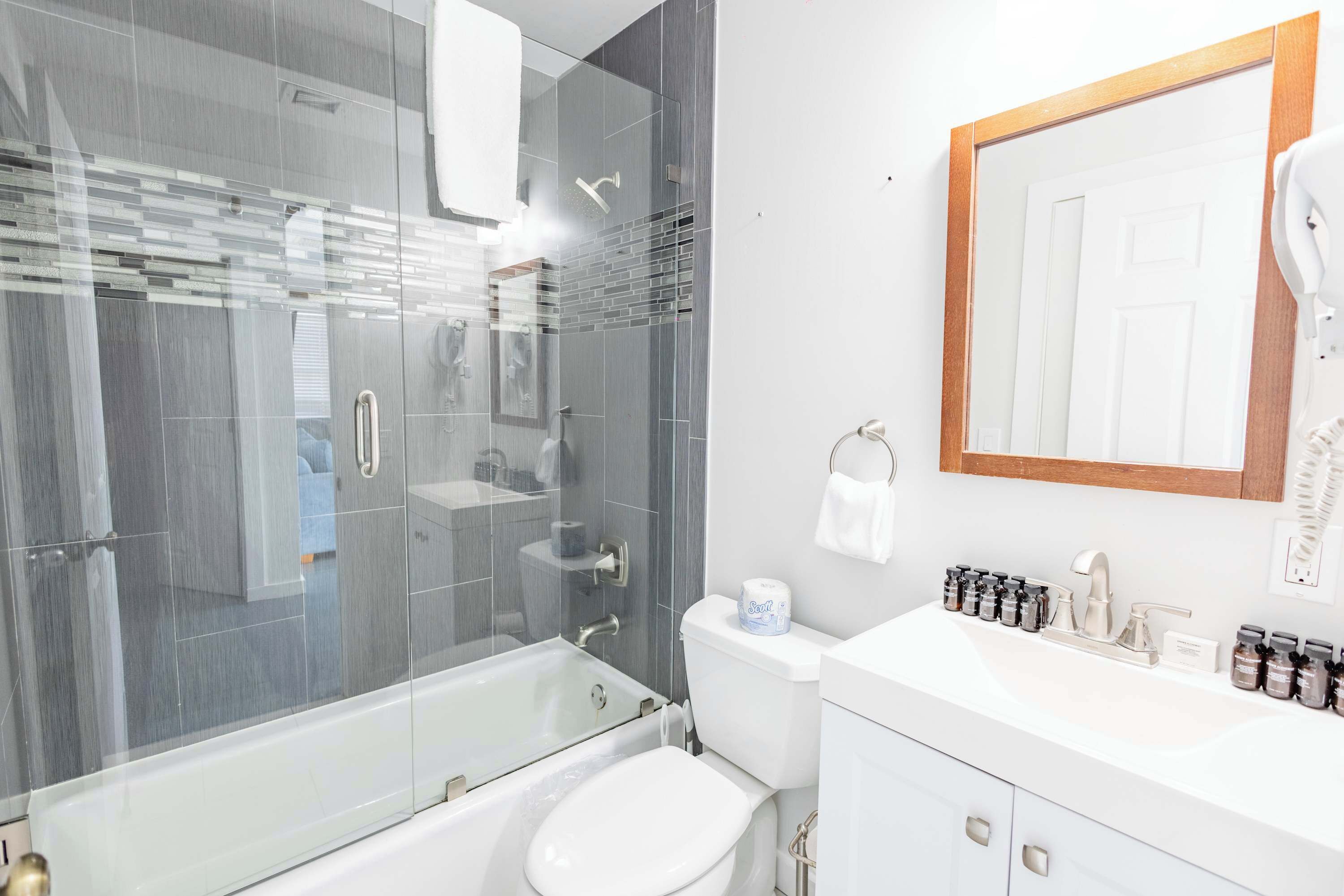 Un baño moderno con ducha de vidrio, inodoro, lavabo con espejo y secador de pelo en la pared.