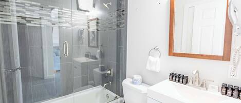 Un baño moderno con ducha de vidrio, inodoro, lavabo con espejo y secador de pelo en la pared.