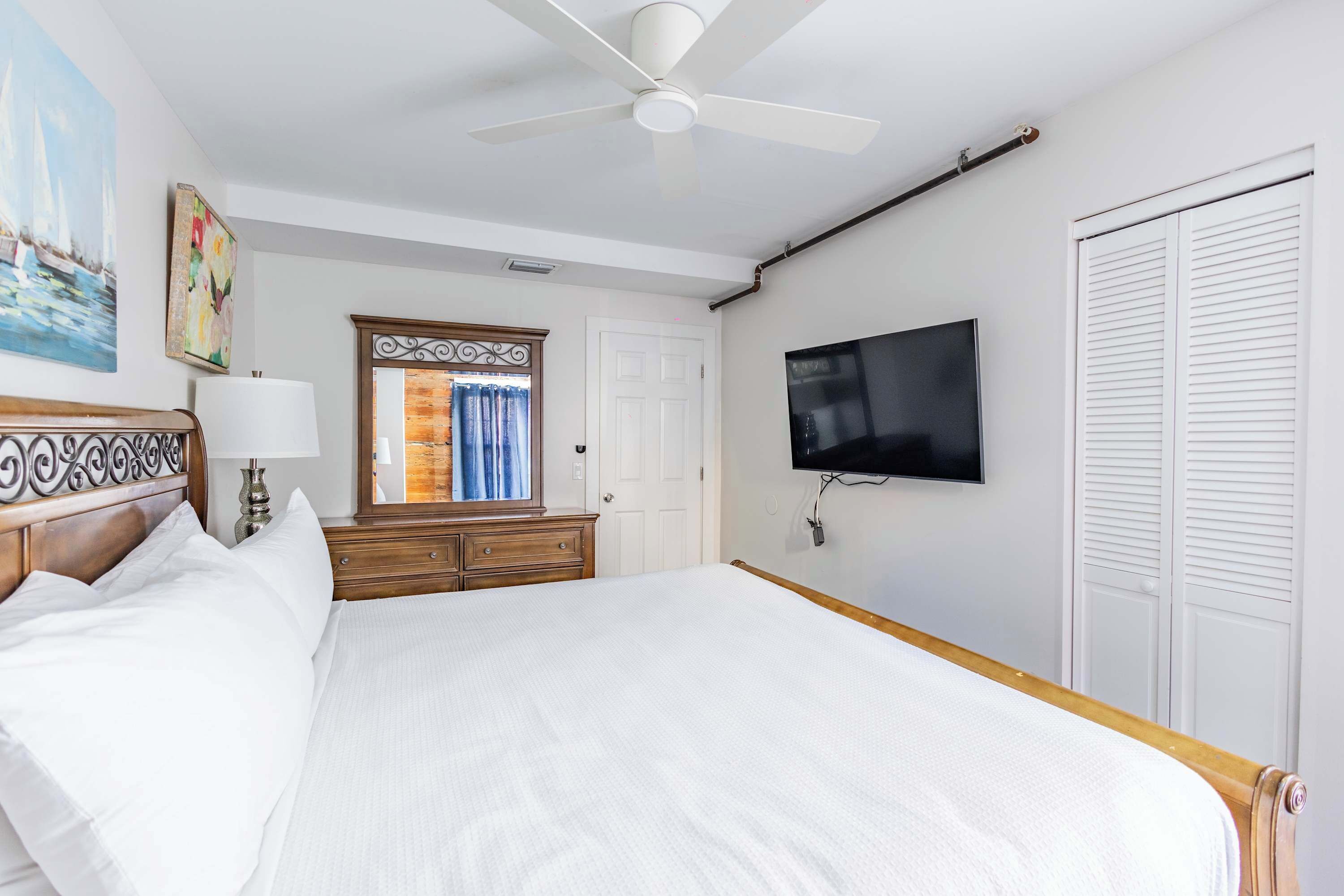 Une chambre d’hôtel avec un lit, une télévision, un ventilateur de plafond, une commode, un miroir et une porte.